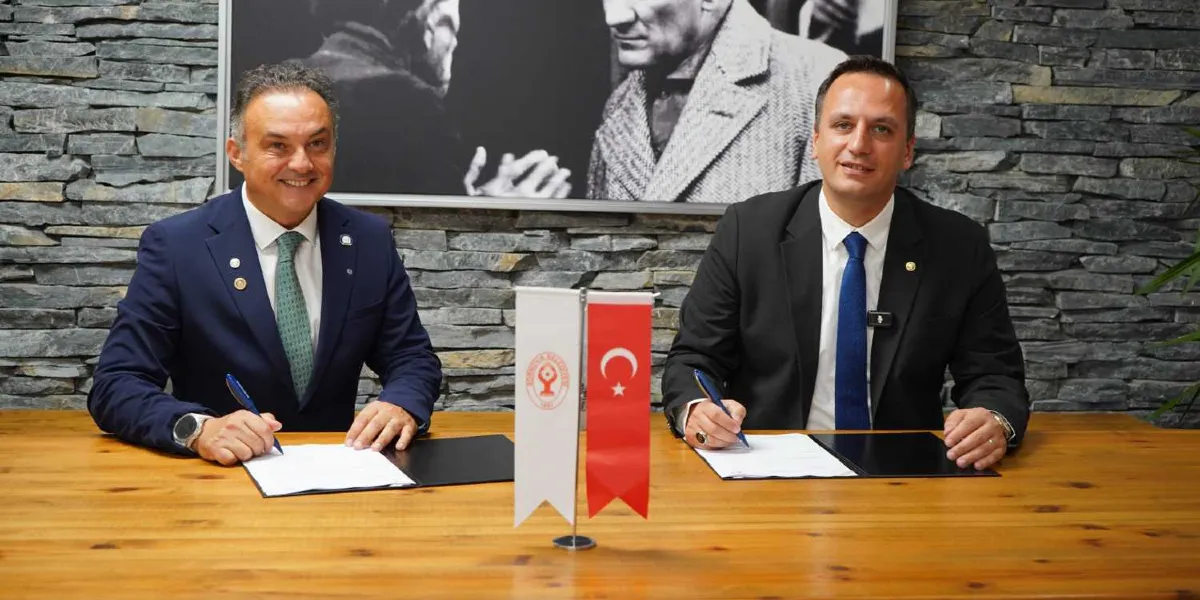 Taş duvarlı bir arka planın önünde, ahşap bir masada yan yana oturan iki erkek, Atık Bank Projesi için hazırlanan protokolü imzalıyor. Masanın ortasında Bornova Belediyesi'nin logosunun bulunduğu beyaz bir flama ile Türk bayrağı yer alıyor. Arka planda ise Mustafa Kemal Atatürk'ün siyah beyaz bir portresi bulunuyor.
