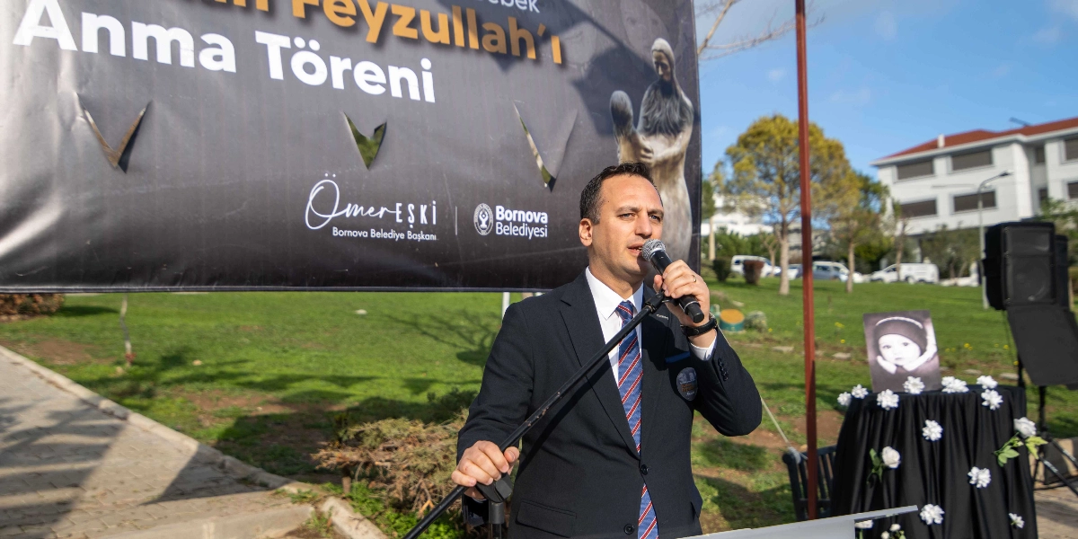Bornova Belediye Başkanı Ömer Eşki, açık havada düzenlenen Türkan Bebek anma töreninde kürsüde mikrofonla konuşma yapıyor. Arkasında 