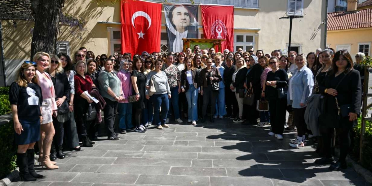 Tarihi bir binanın önünde, arkalarında Türk bayrağı, Mustafa Kemal Atatürk posteri ve Bornova Belediyesi flaması asılı olan, çoğunluğu kadınlardan oluşan kalabalık bir grup, eğitimin geleceği için düzenlenen bir etkinlik kapsamında yan yana duruyor.