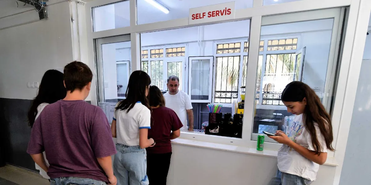 BELGEM binasındaki bir kantin penceresinin önünde sıraya girmiş öğrenciler ve içerideki servis görevlisi. Üzerinde 