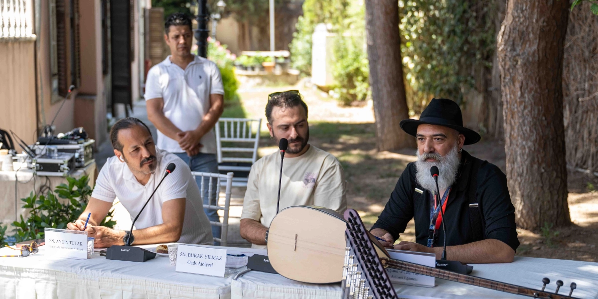 Açık havada, ağaçlık bir alanda düzenlenen bir panelde, masada oturan üç erkek ve ayakta duran bir kişi yer alıyor. Masada oturanlardan en soldaki Aydın Tutak, ortadaki Burak Yılmaz ve en sağda siyah şapkalı, beyaz sakallı bir çalgı yapımcısı bulunuyor. Masanın üzerinde mikrofonlar, isimlikler ve bir adet ud gövdesi ile bağlama sapı duruyor. Katılımcılar, çalgı yapımı üzerine bir söyleşi gerçekleştiriyor.