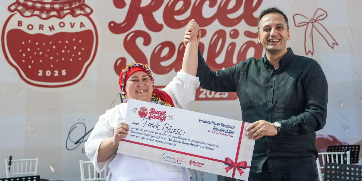 Bornova Reçel Şenliği'nde En Güzel Reçel Yarışması'nda ikincilik ödülü kazanan Feride Güleşçi, ödülünü Bornova Belediye Başkanı Ömer Eşki'nin elinden alıyor. Feride Güleşçi geleneksel kıyafetler ve başında altın süslemeli kırmızı bir örtüyle, Ömer Eşki ise siyah gömleğiyle ödül çekini tutarak gülümsüyor. Arka planda üzerinde 