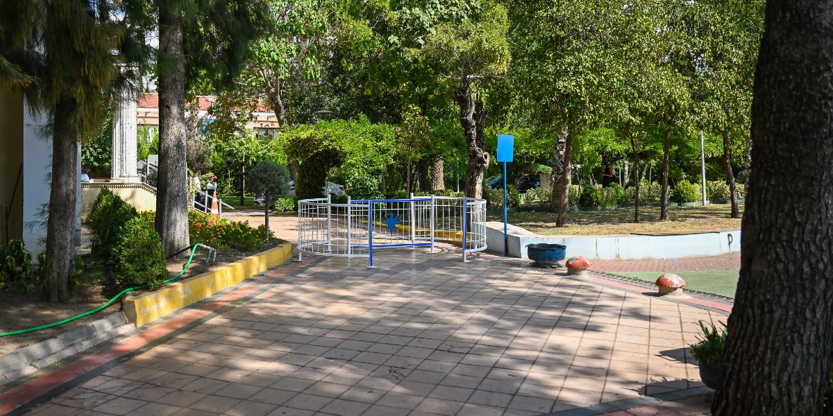 Bornova'da bir parkın yürüyüş yolunda, motosiklet girişini engellemek amacıyla yerleştirilmiş beyaz renkli, yarım daire şeklinde metal bir bariyer bulunuyor. Bariyerin orta kısmında mavi bir yıldız figürü yer alıyor. Parkın çevresi ağaçlar, yeşil alanlar ve çiçeklerle çevrili olup, zemin kiremit rengi kare taşlarla döşenmiş durumda.