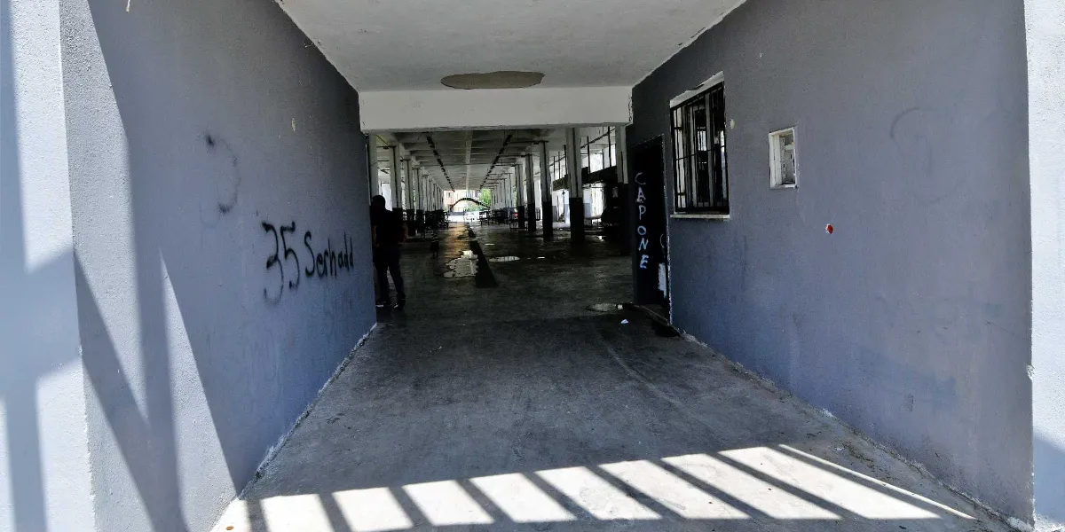 Gri boyalı duvarlara sahip, sütunlu ve uzun bir koridorun girişi. Sol duvarda sprey boya ile yazılmış 