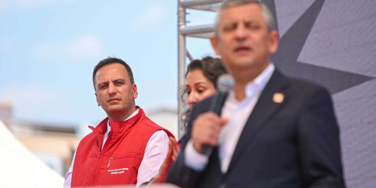 CHP Genel Başkanı Özgür Özel bir kürsüde konuşma yaparken, yanında Bornova Belediye Başkanı Ömer Eşki kırmızı yeleğiyle onu dinliyor.