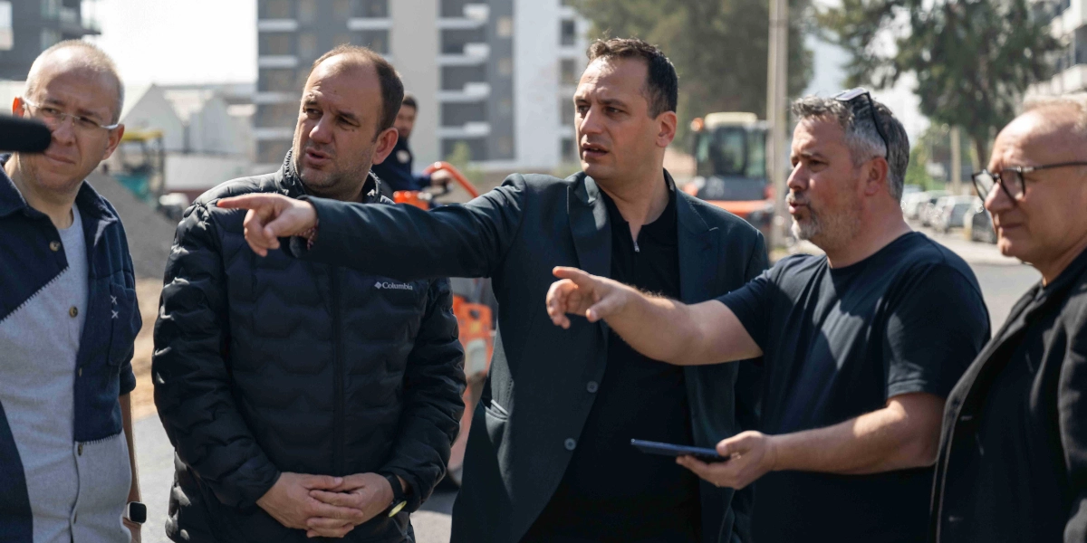 Bornova'da bir şantiye alanında incelemelerde bulunan beş kişilik bir grup erkek, yol çalışmasının yapıldığı bölgeye bakıyor. Gruptaki iki kişi elleriyle ileriye doğru işaret ederek bir şeyler anlatırken, diğerleri onları dinliyor. Arka planda iş makineleri ve devam eden inşaat çalışmaları görülüyor.