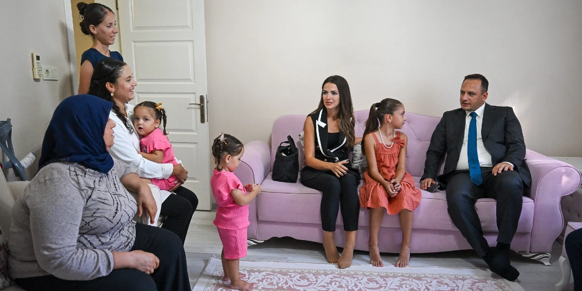 Açık renkli bir odada, pembe bir koltukta oturan takım elbiseli ve kravatlı bir erkek, yanında şık siyah bir kıyafet giyen bir kadın ve turuncu elbiseli bir kız çocuğu ile sohbet ediyor. Koltuğun önünde pembe kıyafetli küçük bir kız çocuğu ayakta dururken, yan tarafta kucağında başka bir çocuk tutan bir kadın ve başörtülü yaşlı bir kadın oturuyor. Arka planda ise ayakta duran bir başka kadın daha bulunuyor.