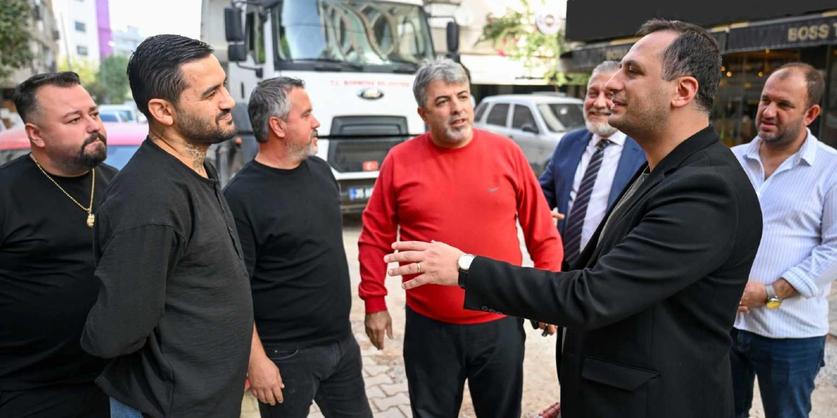 Süvari Caddesi'ndeki yenileme çalışmaları sırasında bir araya gelen altı kişilik bir grup erkek, açık havada sohbet ediyor. Grubun ön planında, siyah ceketli bir adam el hareketleriyle bir şeyler anlatırken, karşısındaki diğer kişiler onu dinliyor. Arka planda ise üzerinde belediye logosu bulunan beyaz bir kamyon ve park halindeki araçlar görülüyor.