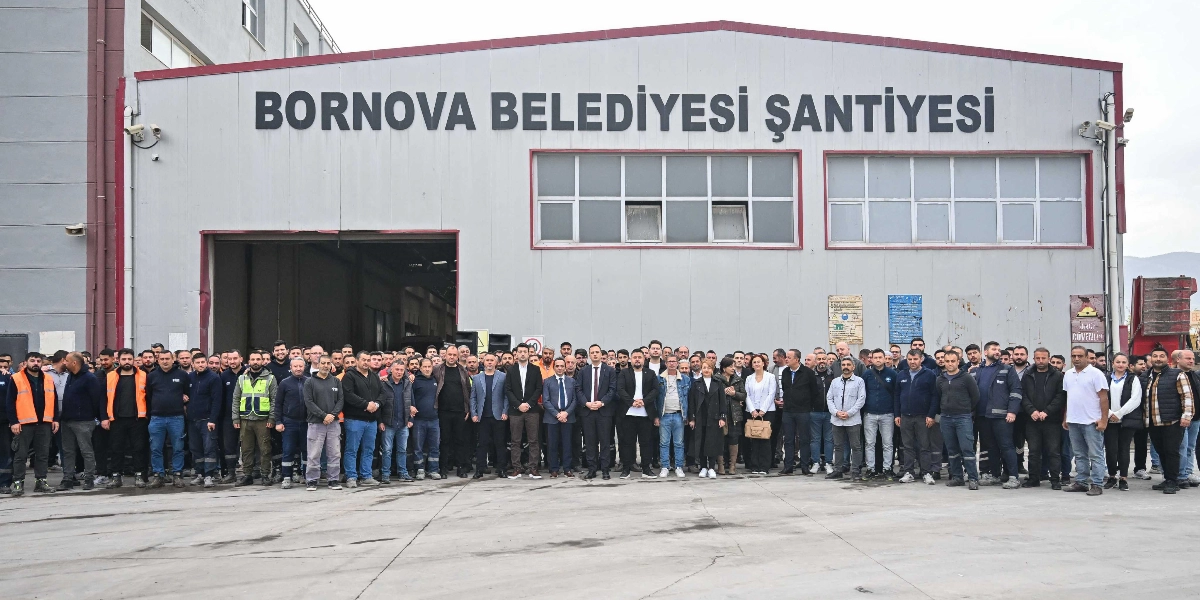 Bornova Belediyesi Şantiyesi binasının önünde yan yana dizilmiş, büyük çoğunluğu erkeklerden oluşan kalabalık bir işçi ve yönetici grubu toplu halde poz veriyor. Arka planda üzerinde büyük harflerle 