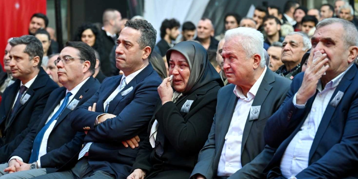 Resmi bir törende yan yana oturan, yakalarında Atatürk fotoğraflı kokartlar bulunan bir grup insan. Ortada siyah başörtülü ve gözyaşı döken bir kadın, yanında ise üzgün ifadeli erkekler yer alıyor. Bazı katılımcılar mendille yüzlerini silerken, arka planda kalabalık bir topluluk görülüyor.