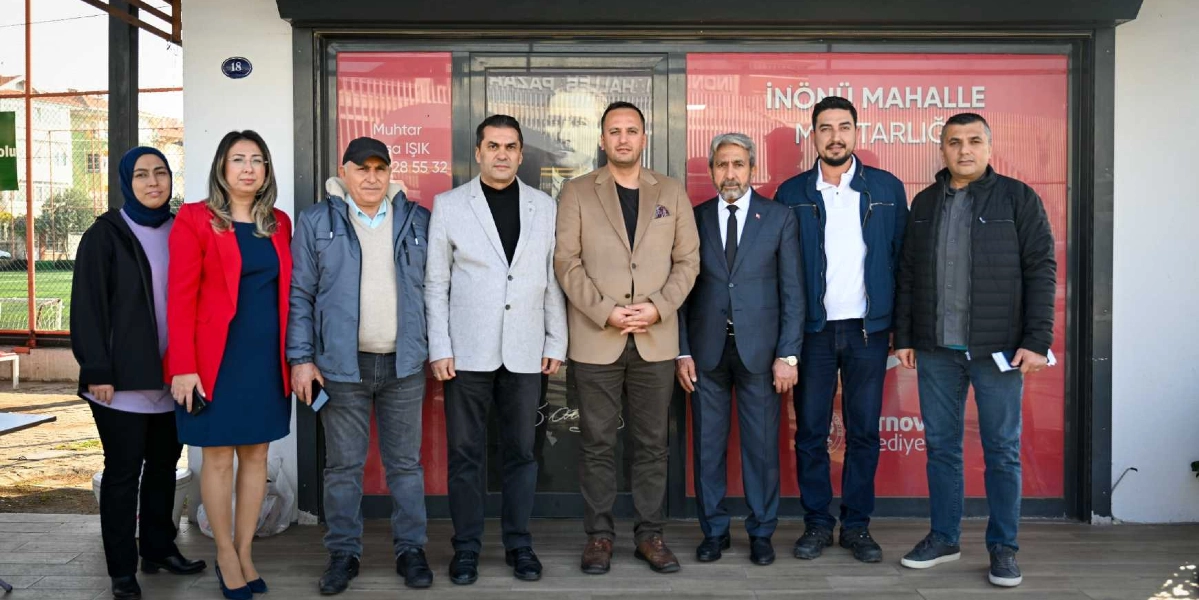 İnönü Mahalle Muhtarlığı binasının önünde yan yana duran, aralarında Bornova Belediye Başkanı Ömer Eşki'nin de bulunduğu sekiz kişilik bir grup. Gruptaki kişiler resmi ve günlük kıyafetlerle poz veriyor. Arka planda kırmızı camlı kapı üzerinde 