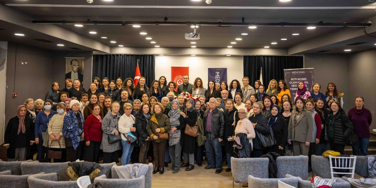 Kapalı bir konferans salonunda, rahim ağzı kanseri farkındalık etkinliği kapsamında bir araya gelmiş kalabalık bir grup kadın ve birkaç erkek katılımcı, objektiflere gülümseyerek poz veriyor. Arka planda Bornova Belediyesi ve Medicana Hastanesi logolarının bulunduğu flamalar, Türk bayrağı ve Mustafa Kemal Atatürk’ün portresi yer alıyor. Sağ taraftaki Medicana standında 