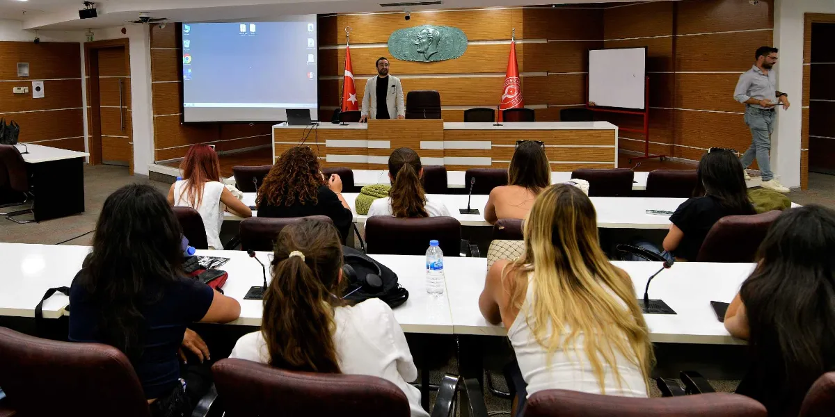 Modern bir konferans salonunda, kürsüde konuşma yapan bir uzmanı dinleyen Peyzaj Mimarlığı öğrencileri. Salonun ön kısmında ahşap panellerle kaplı duvarda Atatürk kabartması, iki yanında Türk bayrağı ve üniversite flaması yer alıyor. Öğrenciler, sıralarda oturmuş şekilde konuşmacıyı takip ediyor, sağ tarafta ise bir kişi ayakta duruyor.