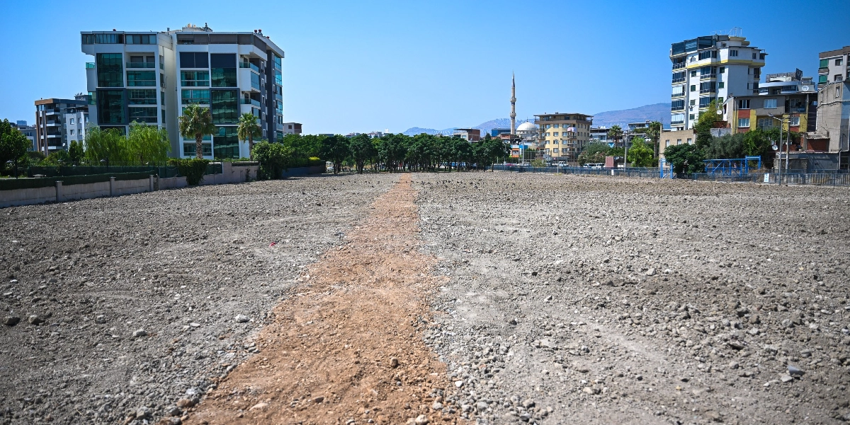Bornova'da etrafı çok katlı apartmanlarla çevrili, ortasından düz bir hat şeklinde toprak yol geçen geniş ve boş bir arazi. Arka planda ağaçlar ve bir cami minaresi görülüyor.