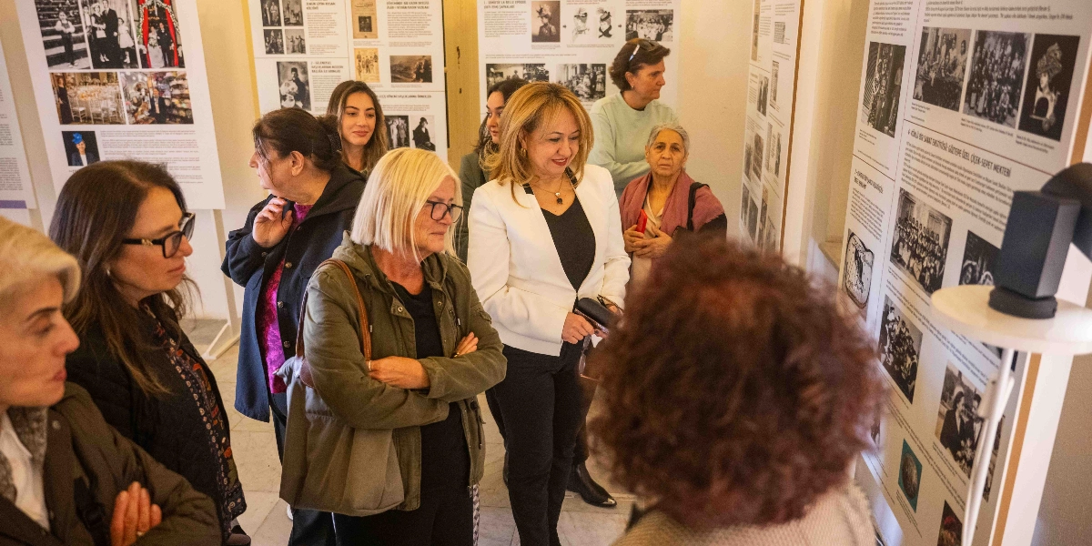 Şapka Devrimi'nin 100. yılına özel düzenlenen sergide, tarihi fotoğraflar ve bilgilendirici metinlerin yer aldığı panoları inceleyen bir grup kadın ziyaretçi. Ziyaretçiler, sergi salonunda yan yana durarak duvardaki belgeleri dikkatle inceliyor.