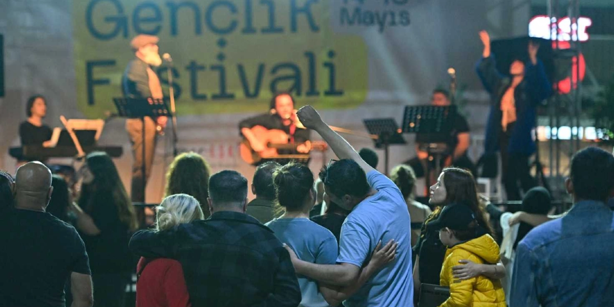 Küçükpark'ta düzenlenen Gençlik Festivali kapsamında, sahnede canlı müzik yapan bir grubun önünde toplanmış kalabalık bir izleyici grubu görülüyor. Sahne arkasındaki dev pankartta 