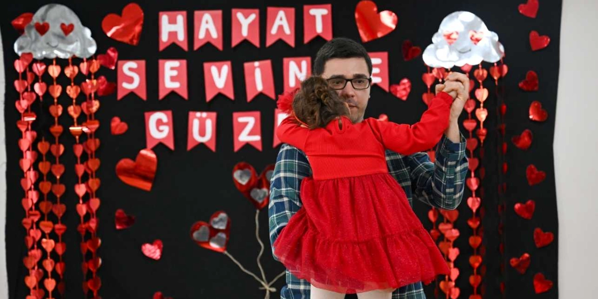 Gözlüklü bir adam, kırmızı elbiseli küçük bir kız çocuğunu kucağında tutarak dans ediyor. Arka planda siyah bir fon üzerinde, üzerinde 