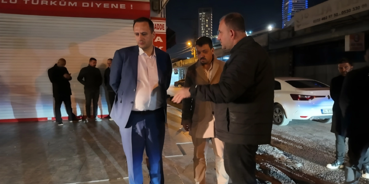 Gece vakti bir sokakta, Bornova'da yürütülen yol çalışmaları kapsamında incelemelerde bulunan bir grup erkek. Ön planda, lacivert takım elbiseli bir kişi, yanında bej ceketli bir adam ve ona bir şeyler anlatan siyah montlu bir kişi yer alıyor. Arka planda ise kapalı kepenkleri olan dükkanlar, park halindeki beyaz bir otomobil ve çevrede bekleyen diğer kişiler bulunuyor.
