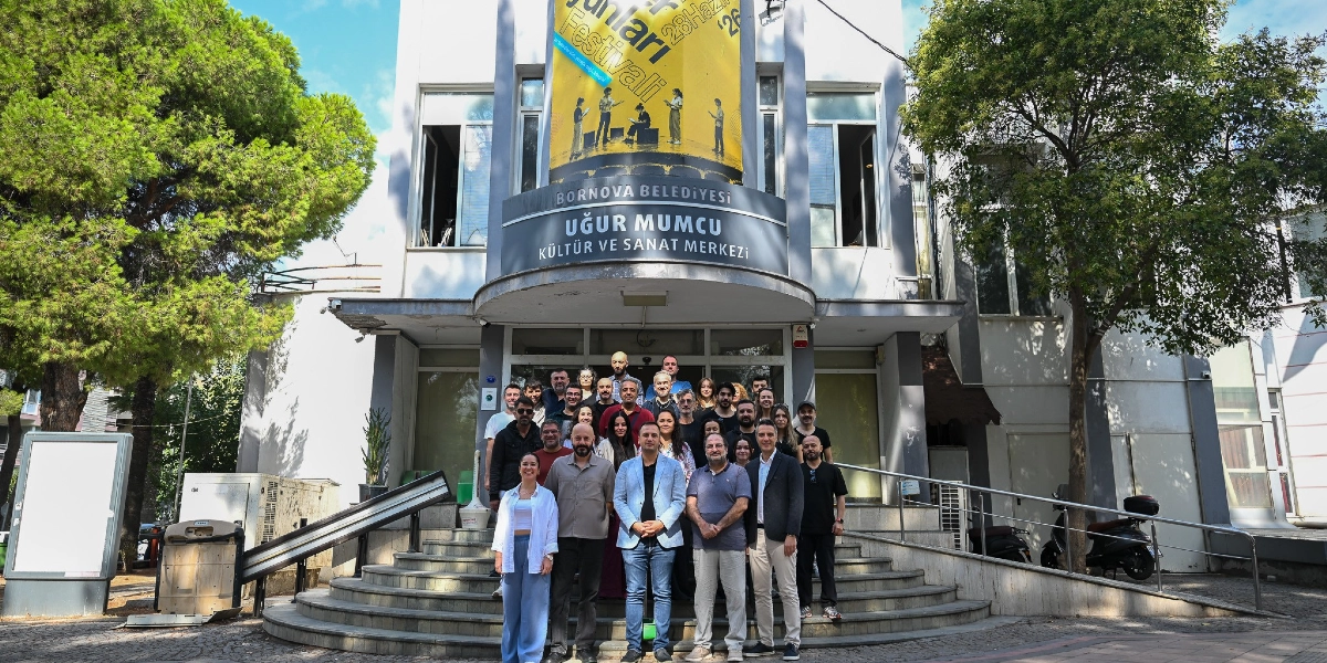 Bornova Belediyesi Uğur Mumcu Kültür ve Sanat Merkezi binasının önündeki merdivenlerde toplanmış, yeni sezonu karşılayan kalabalık bir tiyatro ekibi. Binanın cephesinde 