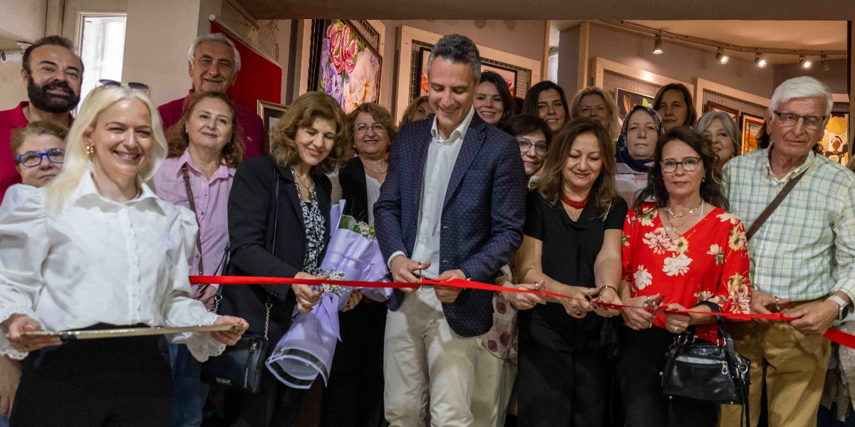 Bir sanat galerisinde, Paletimdeki Renkler sergisinin açılış kurdelesini kesen bir grup insan. Ortada lacivert ceketli bir erkek ve yanında siyah kıyafetli, elinde çiçek buketi tutan bir kadın ile kırmızı çiçek desenli bluz giyen bir kadın, ellerindeki makaslarla kırmızı kurdeleyi kesiyor. Çevredeki diğer katılımcılar gülümseyerek bu anı izliyor, arka planda ise duvarda asılı tablolar görülüyor.