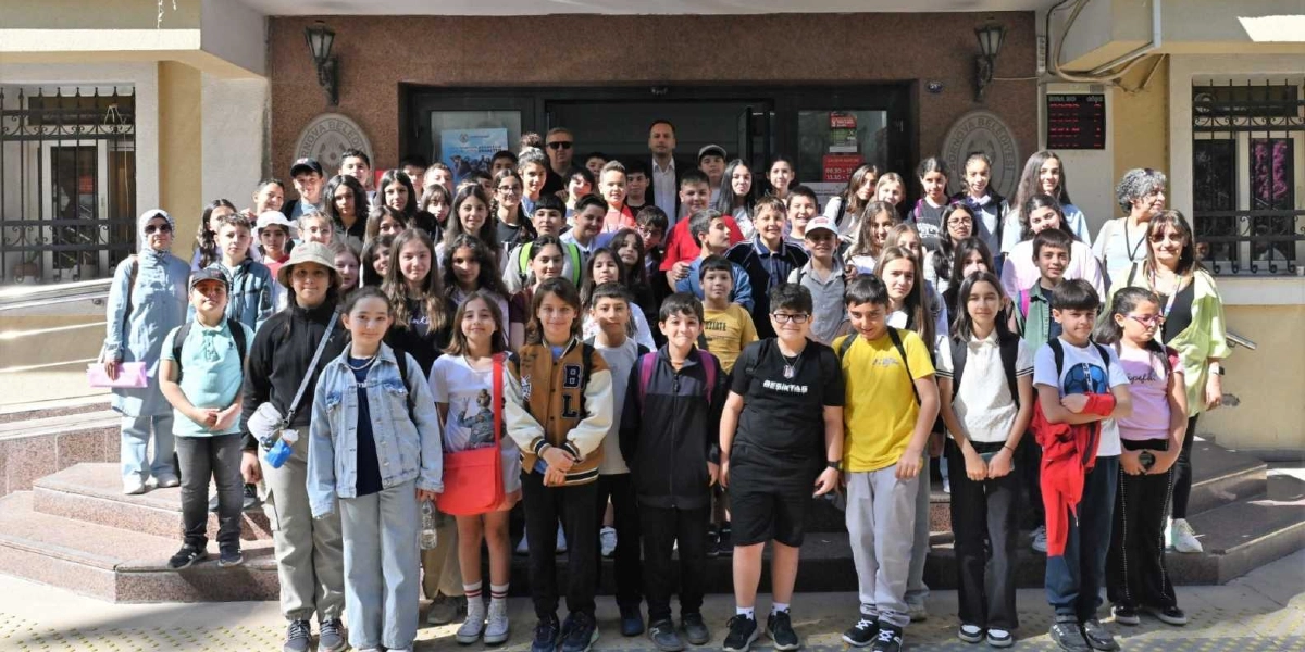 Bornova Belediyesi binasının girişinde, merdivenlerde yan yana dizilmiş kalabalık bir öğrenci grubu ve onlara eşlik eden yetişkinler objektife gülümsüyor. Ortaokul çağlarında olduğu görülen öğrenciler, günlük kıyafetleriyle binanın önünde toplu bir hatıra fotoğrafı çektiriyor.