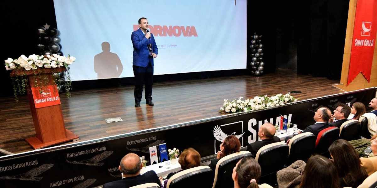 Konferans salonunda sahne üzerinde mavi ceketli bir erkek konuşma yaparken, izleyiciler koltuklarda oturarak onu dinliyor. Sahnenin solunda üzerinde Sınav Koleji logosu bulunan bir kürsü, arkasında ise üzerinde büyük harflerle 
