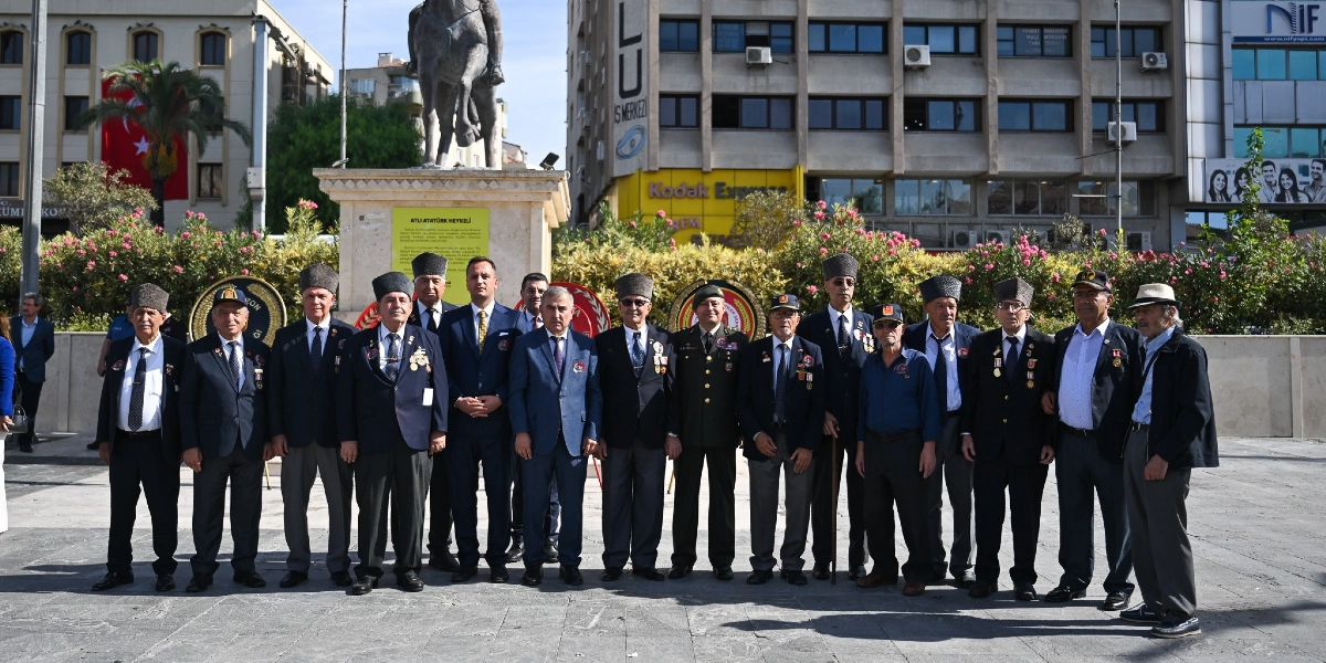 Bornova'daki Atatürk heykeli önünde yan yana dizilmiş, bir kısmı kalpaklı ve madalyalı gaziler ile sivil yetkililerden oluşan bir grup, 19 Eylül Gaziler Günü anma töreni kapsamında poz veriyor.