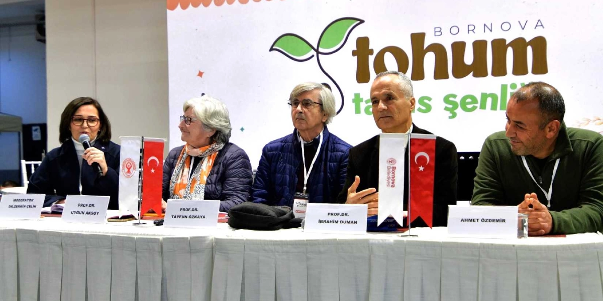 Bornova Tohum Takas Şenliği kapsamında düzenlenen panelde, beyaz örtülü bir masada yan yana oturan beş konuşmacı yer alıyor. Soldan sağa doğru sırasıyla; moderatör Dr. Zerrin Çelik, Prof. Dr. Uygun Aksoy, Prof. Dr. Tayfun Özkaya, Prof. Dr. İbrahim Duman ve Ahmet Özdemir bulunuyor. Konuşmacıların önünde isimlerinin yazılı olduğu kartlar, Bornova Belediyesi logolu küçük bayraklar ve Türk bayrakları yer alıyor. Arka planda ise üzerinde 