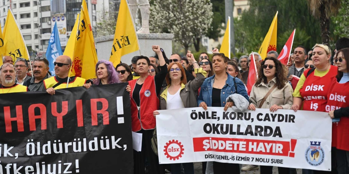 Bornova'da düzenlenen bir eylemde, ellerinde pankartlar taşıyan ve yumruklarını havaya kaldıran bir grup insan yer alıyor. Soldaki siyah pankartta büyük harflerle 