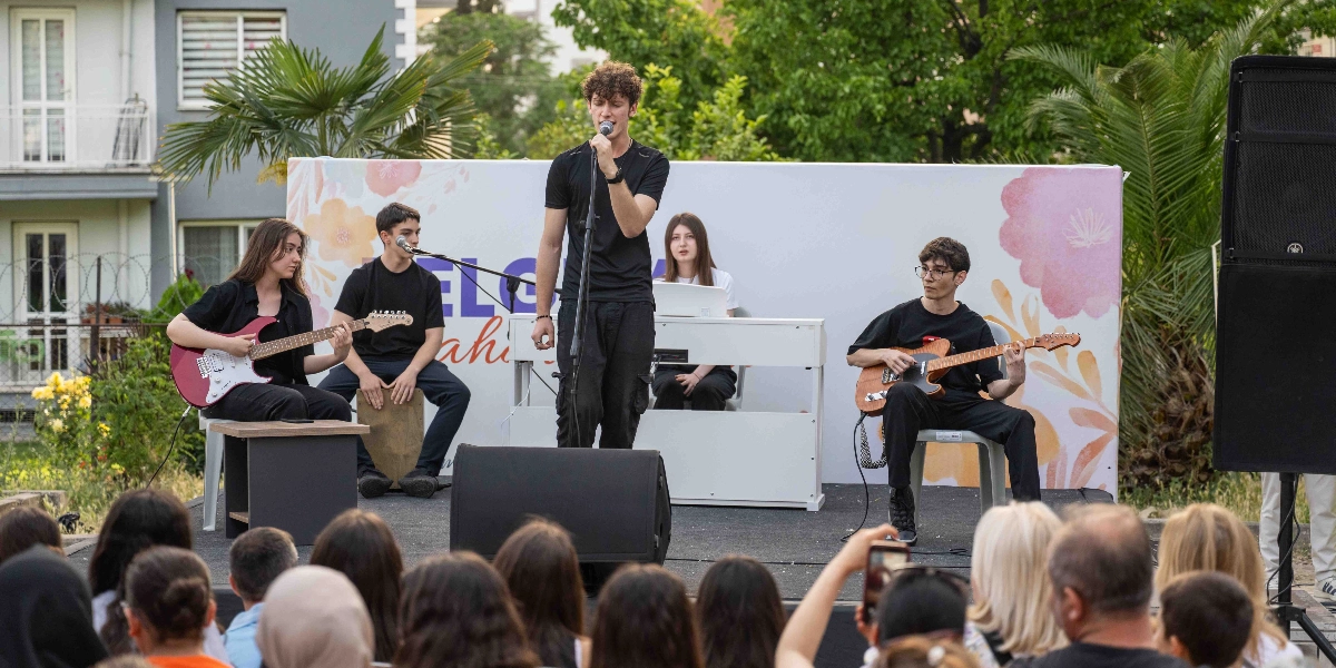 Açık havada kurulan bir sahnede müzik yapan beş kişilik genç bir grup, izleyicilere konser veriyor. Grubun merkezinde ayakta şarkı söyleyen bir solist, sol tarafta elektro gitar çalan bir genç kız, yanında perküsyon çalan bir genç, sağ tarafta ise elektro gitar çalan gözlüklü bir genç ve arkada beyaz bir dijital piyano çalan bir genç kız bulunuyor. Sahnenin arka planında üzerinde çiçek desenleri ve 