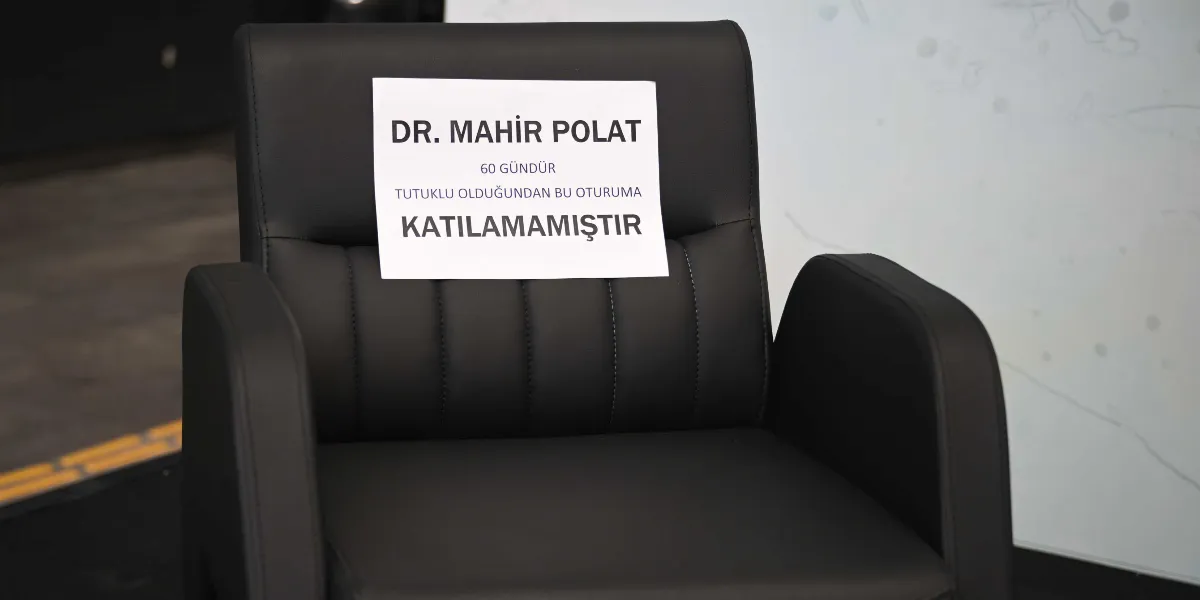 Üzerinde Dr. Mahir Polat 60 gündür tutuklu olduğundan bu oturuma katılamamıştır yazılı bir kağıdın asılı olduğu boş siyah deri koltuk.
