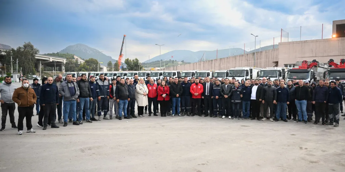 Açık havada, arkalarında sıralanmış çok sayıda kamyonun bulunduğu geniş bir alanda toplanmış, aralarında Başkan Ömer Eşki'nin de yer aldığı kalabalık bir işçi grubu yan yana durarak poz veriyor.