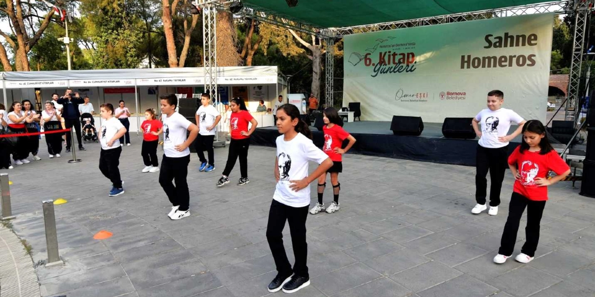 Bornova Belediyesi tarafından düzenlenen 6. Kitap Günleri kapsamında, üzerinde Atatürk baskılı beyaz ve kırmızı tişörtler giyen bir grup çocuk, açık hava sahnesinin önündeki alanda dans gösterisi sergiliyor. Arka planda 