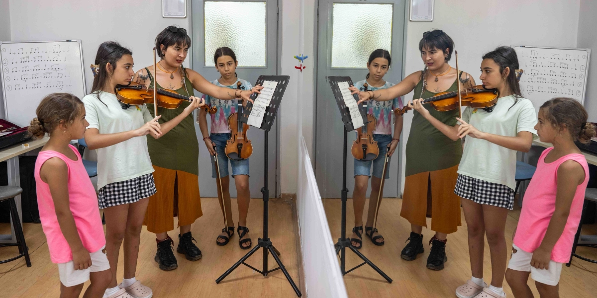 Bir müzik sınıfında, eğitmen eşliğinde keman eğitimi alan üç kız çocuğu ve eğitmenleri yer alıyor. Eğitmen, elinde keman tutan bir öğrenciye nota sehpası üzerindeki notaları gösterirken, diğer iki öğrenci ellerinde kemanlarıyla onları izliyor. Odanın ortasındaki büyük bir ayna, sınıftaki kişilerin ve ortamın yansımasını oluşturuyor. Arka planda duvarda asılı beyaz tahtalarda nota çalışmaları yazılı.