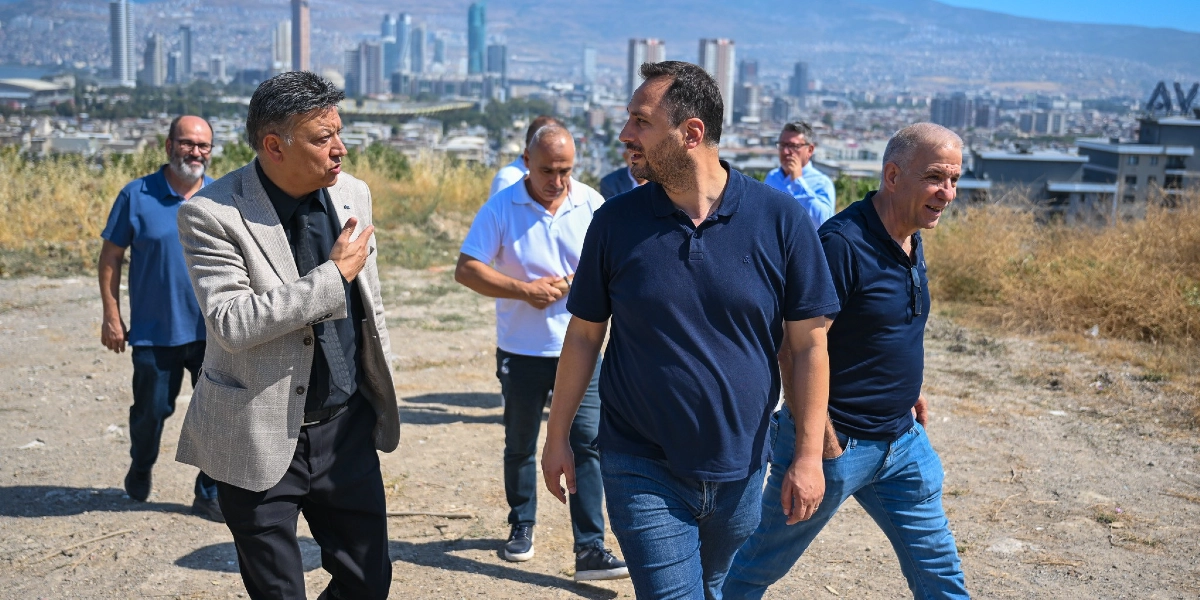 Beş kişilik bir grup, arkalarında İzmir şehir manzarası bulunan yüksek ve boş bir arazide yürürken sohbet ediyor. Önde, gri ceketli bir adam yanında yürüyen lacivert tişörtlü bir adamla konuşuyor; arkalarında ise beyaz tişörtlü, mavi gömlekli ve lacivert tişörtlü diğer üç kişi onları takip ediyor.