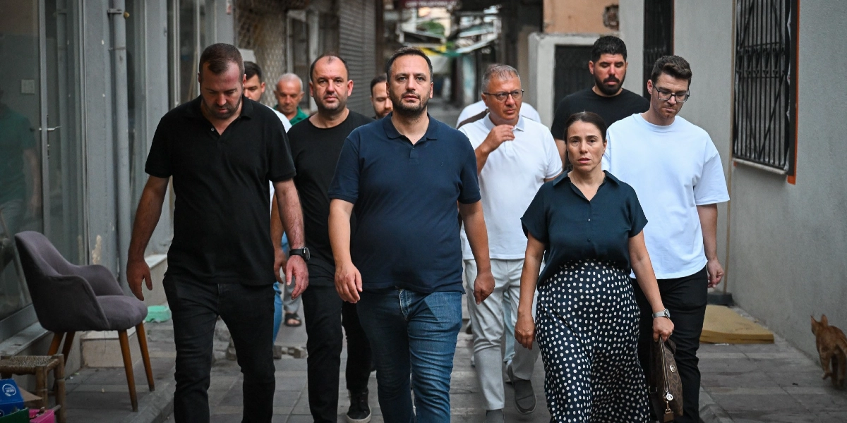 Çamdibi sokaklarında yürüyen, aralarında Bornova Belediye Başkanı Ömer Eşki'nin de bulunduğu bir grup yetkili ve çalışma arkadaşı, bölgedeki altyapı çalışmalarını incelemek üzere ilerliyor.