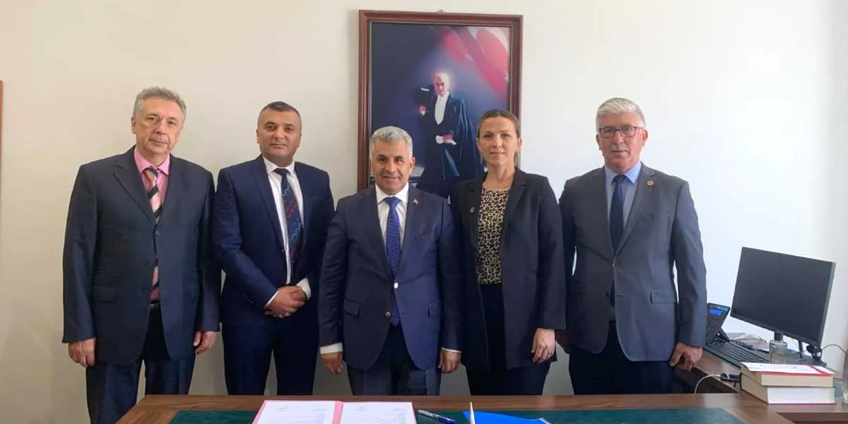 Ofis ortamında yan yana duran, takım elbiseli dört erkek ve bir kadından oluşan grup. Arka planda duvarda Mustafa Kemal Atatürk'ün cübbeli bir portresi asılıdır. Önlerinde üzerinde belgelerin bulunduğu bir çalışma masası yer almaktadır.