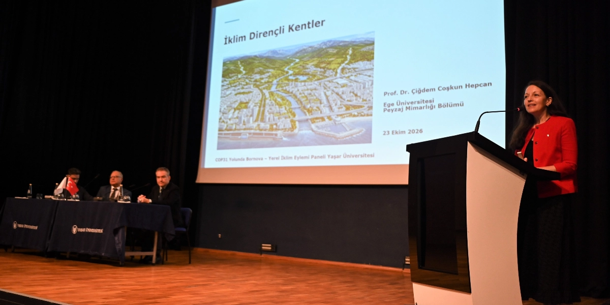 Yaşar Üniversitesi'nde düzenlenen COP31 Yolunda Bornova - Yerel İklim Eylemi Paneli'nde, kürsüde konuşma yapan Prof. Dr. Çiğdem Coşkun Hepcan yer alıyor. Arkasındaki dev ekranda 