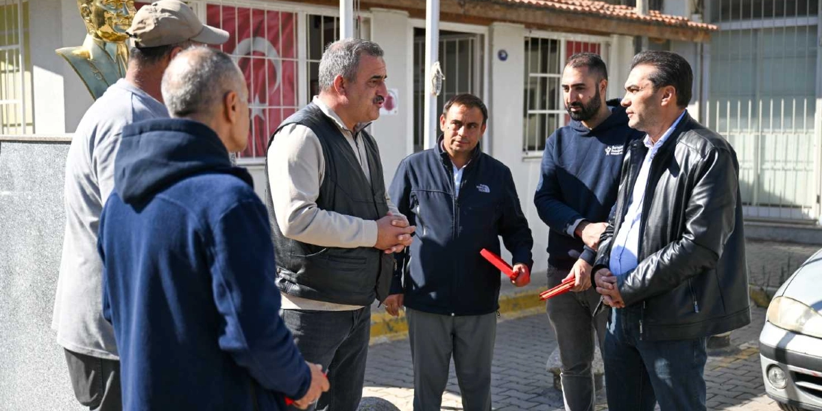 Açık havada, bir binanın önünde bir araya gelmiş altı kişilik bir grup erkek, birbirleriyle sohbet ediyor. Grubun sol tarafında arkası dönük olanlar ve ortada konuşan, ellerini kavuşturmuş gri saçlı bir adam bulunuyor. Sağ tarafta ise ellerinde kırmızı dosyalar tutan iki kişi ve onlara eşlik eden, siyah deri ceketli bir başka kişi yer alıyor. Arka planda Atatürk büstü ve Türk bayrağı görülüyor.