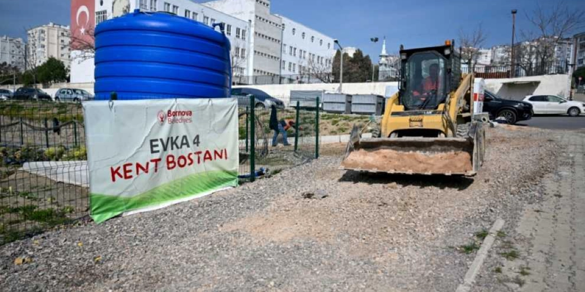 Bornova Belediyesi'ne ait Evka 4 Kent Bostanı tabelasının yanında büyük mavi bir su deposu ve toprak zeminde çalışan sarı renkli bir iş makinesi bulunuyor. Arka planda ise üzerinde Türk bayrağı asılı olan beyaz bir bina ve şehir yerleşimi görülüyor.