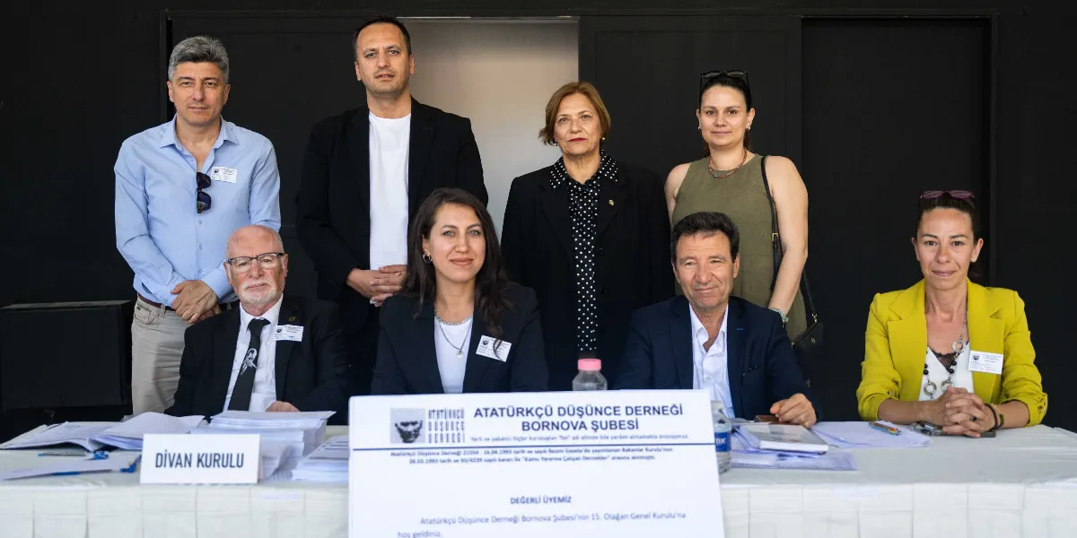 Atatürkçü Düşünce Derneği Bornova Şubesi 15. Olağan Genel Kurulu'nda, üzerinde dernek logosu ve bilgileri bulunan bir masanın arkasında yan yana duran ve oturan dokuz kişilik grup. Masanın üzerinde 