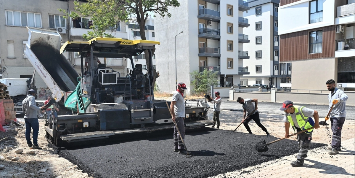 Bornova'da bir sokakta asfalt serim çalışması yapan işçiler ve Vögele marka asfalt serme makinesi. İşçiler ellerindeki küreklerle taze dökülen asfaltı düzeltirken, arka planda modern apartmanlar ve çalışma yapan bir kamyon görülüyor.