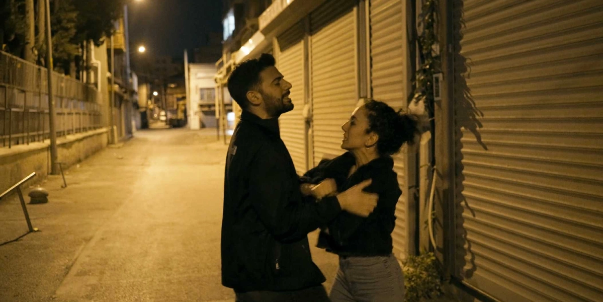 Gece vakti, kepenkleri kapalı dükkanların bulunduğu boş bir sokakta, siyah ceketli bir erkek ve siyah ceketli bir kadın yüz yüze durmuş, hararetli bir şekilde tartışıyor.