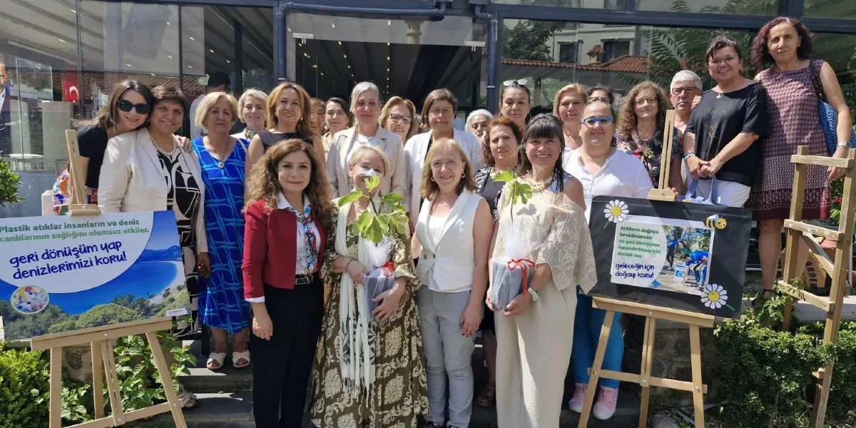 Çevre bilinci oluşturmak amacıyla bir araya gelmiş, çoğunluğu kadınlardan oluşan kalabalık bir grup, dış mekanda yan yana durarak poz veriyor. Grubun önünde, ahşap şövaleler üzerinde iki adet bilgilendirme panosu yer alıyor. Sol taraftaki panoda 