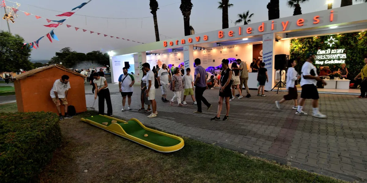 Uluslararası İzmir Fuarı alanında yer alan Bornova Belediyesi standının önünde, ziyaretçilerin gezindiği ve vakit geçirdiği bir akşamüstü manzarası. Standın üzerinde büyük harflerle 