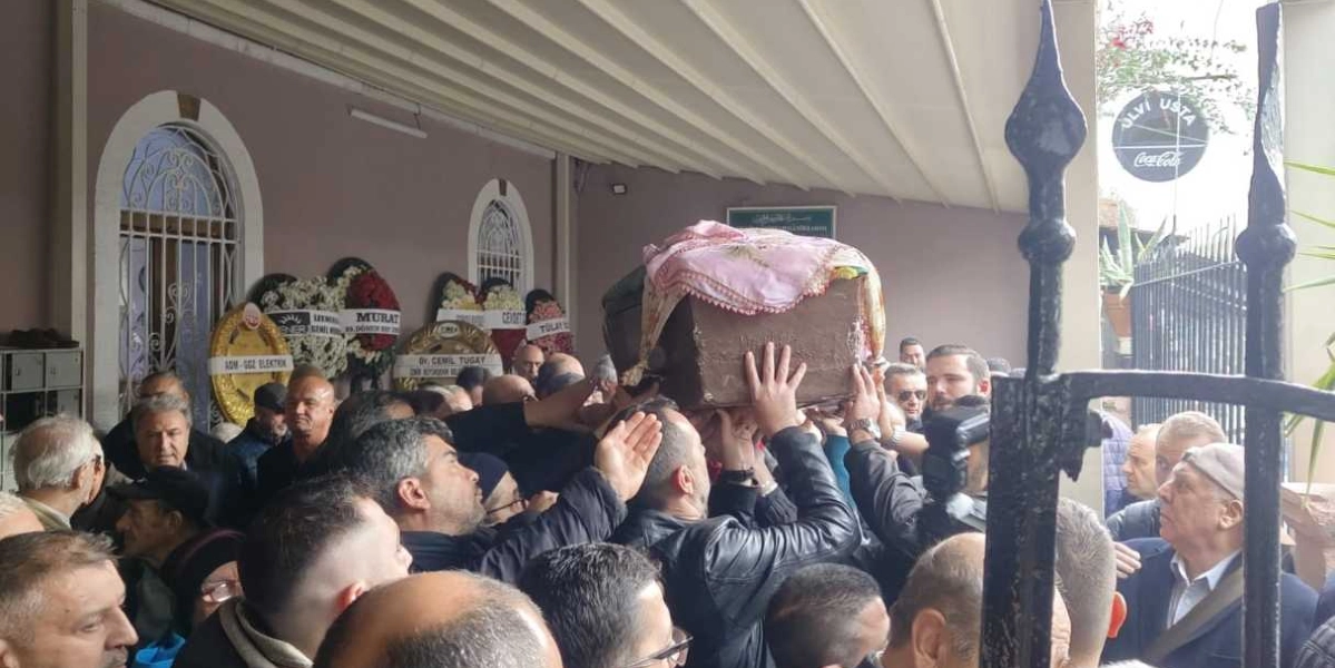 Kalabalık bir grup insanın, üzerinde pembe bir örtü bulunan tabutu omuzlarında taşıyarak bir binadan çıkardığı cenaze töreni.