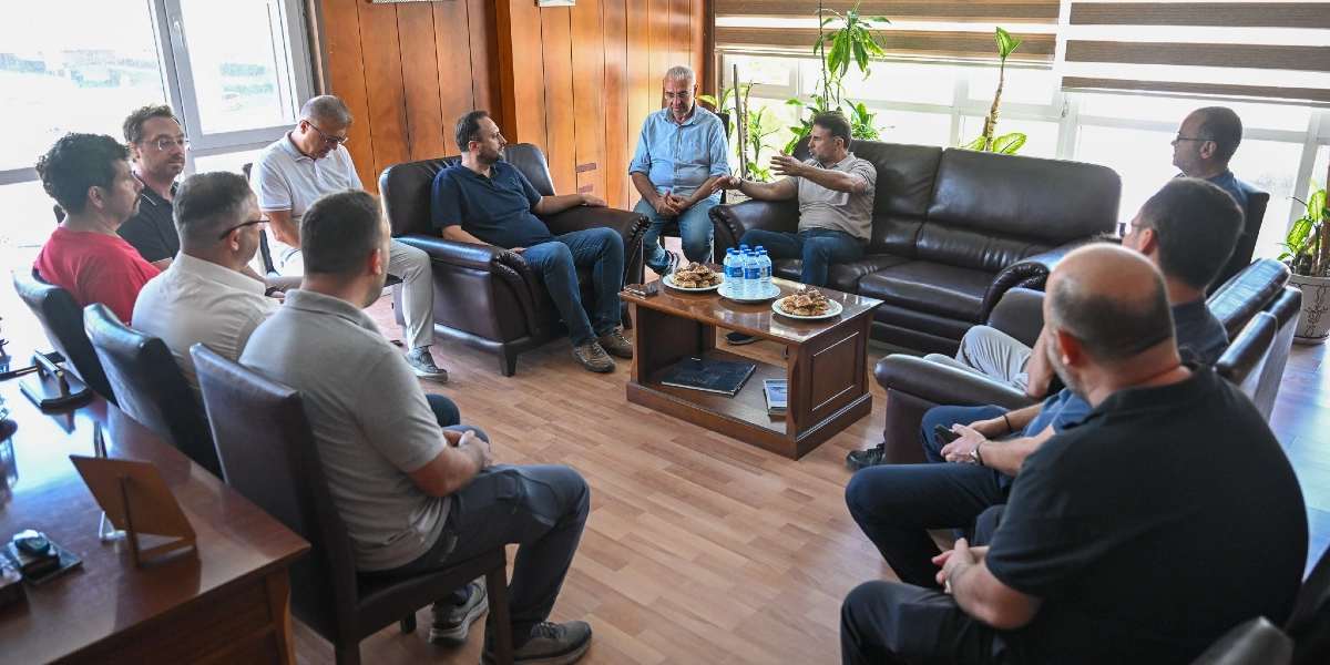Bornova Belediye Başkanı Ömer Eşki, 3. Sanayi Sitesi'nde bir grup esnaf ve yönetici ile ofis ortamında bir araya gelerek sohbet ediyor. Toplantı masasında ikramlıklar ve su şişeleri bulunurken, katılımcılar karşılıklı koltuklarda oturarak fikir alışverişinde bulunuyor.