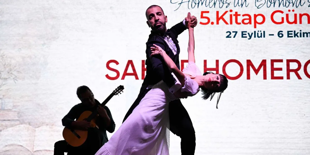 Siyah takım elbiseli bir erkek ve beyaz elbiseli bir kadının tango yaptığı, arka planda ise gitar çalan bir müzisyenin yer aldığı sahnede, üzerinde 