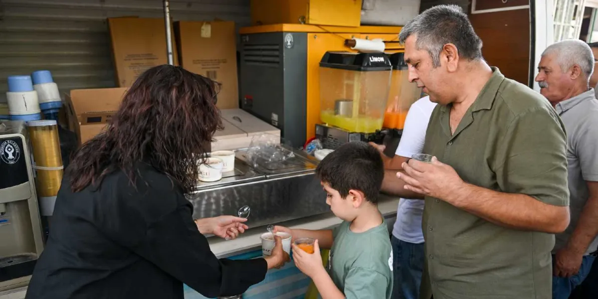 Bornova Belediyesi logolu bir ikram aracında, siyah kıyafetli bir görevli küçük bir çocuğa ve yanındaki yetişkinlere bardaklarda içecek ve dondurma ikram ediyor. Arka planda limonata makineleri ve çeşitli ekipmanlar yer alıyor.