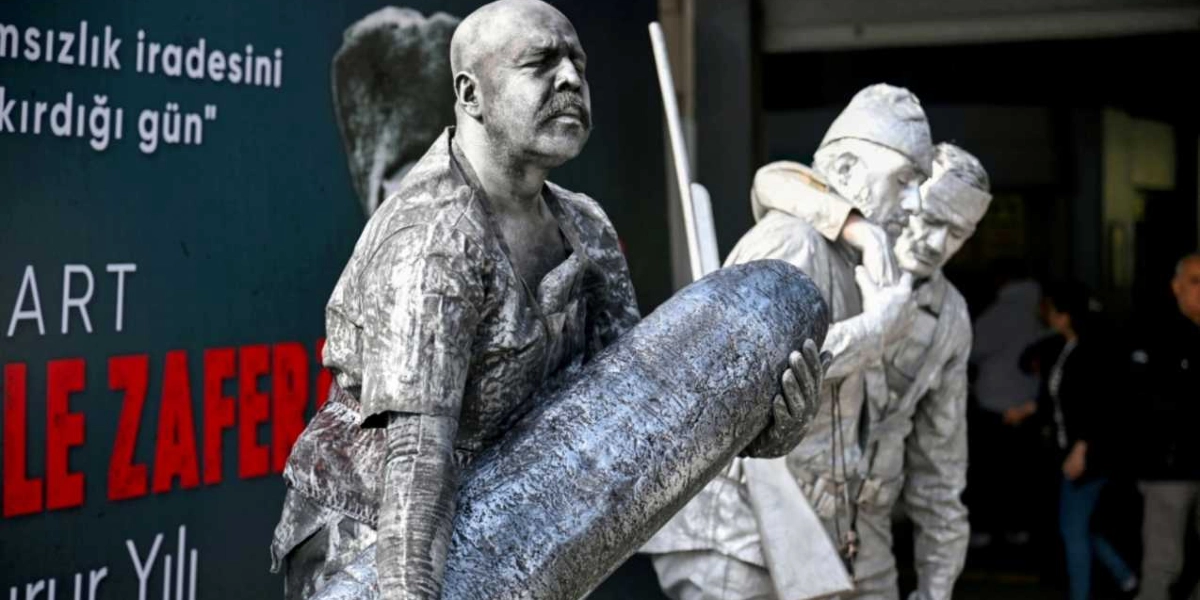 Çanakkale Savaşı'nı canlandıran, vücutları ve kıyafetleri gümüş rengine boyanmış üç sokak sanatçısı. Öndeki sanatçı büyük bir top mermisini sırtlanmış şekilde yürürken, arkasındaki iki sanatçı yaralı bir askeri taşıyormuş gibi poz veriyor. Arka planda üzerinde 